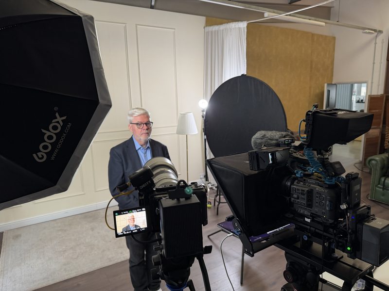 John Elliott recording a video course in a studio, framed by a broadcast camera and softbox lighting.